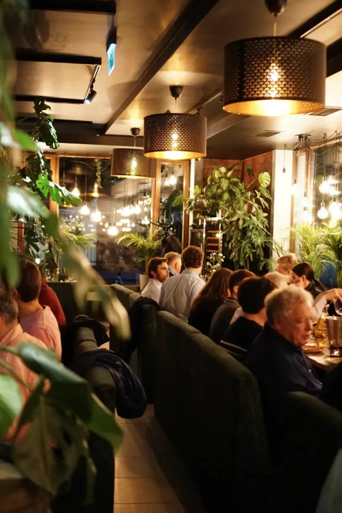 Wnętrze restauracji podczas przyjęcia – rząd zielonych kanap ustawionych tyłem, wypełnione gośćmi, ujętych w trakcie jedzenia, rozmawiania, śmiechu.