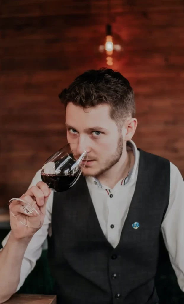 A young man raises a glass of red wine to his lips.